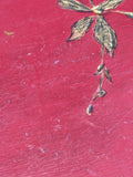 Macro detail of the Chinoiserie tabletop showing a gilt dragonfly motif with outstretched wings and a trailing stem with small lance-shaped leaves, painted on the red ground.