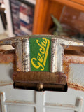 Close-up of Gescha maker’s label in yellow script on green background on toy car axle