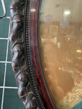Close-up detail of the left side of the oval mahogany frame showing the wide carved acorn and leaf relief border and inner beaded moulding.