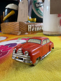 Three-quarter front view of vintage red US-Zone Germany tin litho toy car on yellow fabric