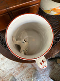 Overhead view into an antique Staffordshire surprise mug showing the spotted ceramic frog at the base