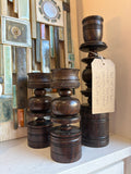 Set of three turned-wood candelabras on a shelf in front of a ceramic wall hanging 
