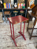 Front-on view of the Chinoiserie side table apron showing a repeating gilt diamond lattice pattern on red ground, gilded top edge, and the four red faux bamboo legs with gold ring detailing at the joints.