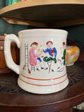 Front view of an antique Staffordshire frog mug with hand-painted folk art figures and orange line decoration