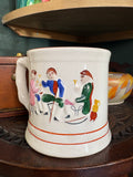 Side view of a large antique Staffordshire surprise mug showing hand-painted figures in pink, blue, and green