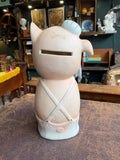 Rear view of bisque pig money bank showing plain pink body, coin slot at back of head and blue-striped dungarees.