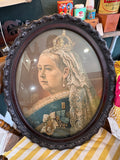 Large oval Victorian portrait chromolithograph of Queen Victoria in a carved mahogany frame with glass, showing the Queen in three-quarter profile wearing crown, lace veil, Garter sash, Royal Victorian Order badge with Prince Albert cameo medallion, and lace mantle.