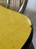 Close-up of chair seat corner showing a small chip to the black Formica edge trim.