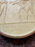 Detail of soldiers’ legs and outstretched arm on the wax relief medallion
