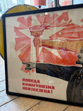 Close-up of the left side of the framed Konuhov poster, showing the flaming torch topped with a hammer and sickle emblem held aloft by a fist, surrounded by bold red radiating lines, with Lenin's outstretched pointing arm below and the full Cyrillic slogan "Победа коммунизма неизбежна!" prominently displayed.