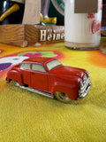 Side view of vintage red tin litho toy car marked Made in US-Zone Germany, c.1945–1952, on yellow fabric