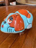 Vintage tin wind-up dog toy viewed from the side, showing body shape and wind-up key.