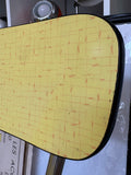 Close-up of yellow woven-pattern Formica chair back showing texture and black edge trim.
