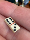 Close-up of hand holding a single miniature bone domino tile