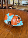 Vintage tin wind-up dog toy on a wooden table, three-quarter view showing full body and key.