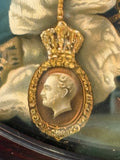 Extreme close-up of the Royal Victorian Order badge depicted in the Queen Victoria portrait, showing the oval gold-framed cameo with a profile portrait of Prince Albert surmounted by a royal crown, rendered in fine chromolithographic detail.
