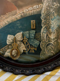 Close-up of the lower central section of the Queen Victoria portrait, showing her blue Garter sash, white silk bow, jewelled bar brooch, the Royal Victorian Order badge with crowned cameo medallion, and a second cross-shaped order badge.
