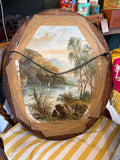 Reverse of the oval Victorian portrait frame showing the original aged brown paper backing, black cord hanging wire on two metal ring fixings, and a partial view of a Victorian landscape print used as backing material.