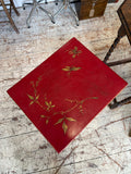 Overhead view of the red painted rectangular tabletop showing gilt Chinoiserie decoration including a flowing botanical stem with pointed leaves, two dragonflies, and a small butterfly on a crimson ground.