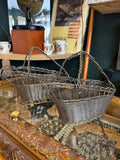 Two vintage silver-plated woven wire wine baskets with twisted rope handles on a display case 