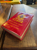 Red vinyl-covered "Little Red Book" of Mao quotations resting on a wooden table, cover visible.