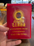 Little Red Book" of Mao quotations held in hand, showing gold cover lettering and Mao portrait medallion.