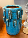 Angled view of a turquoise vase showing the rolled rim, unglazed terracotta interior and raised block decoration