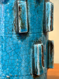 Close-up of fine crackle in a turquoise glaze, with raised blocks showing the dark body at their edges